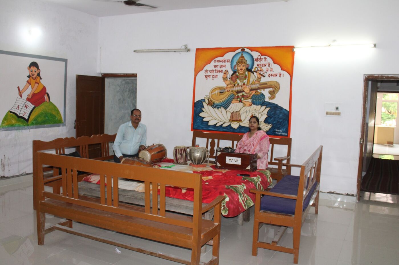 Reception hall with a painted mural of Maa Saraswati and a staff member at the desk