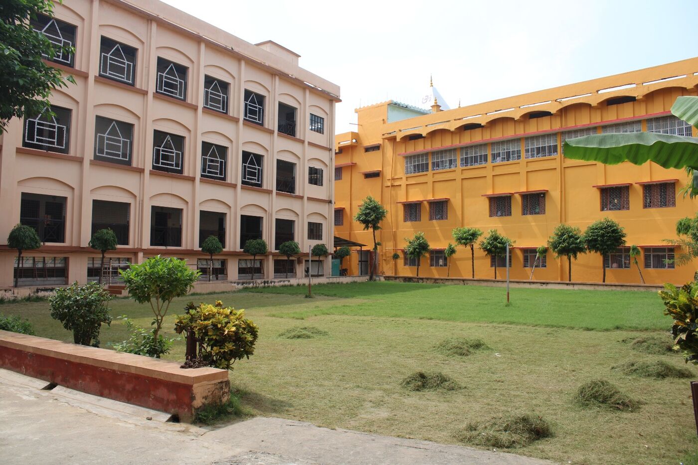Garden and lawn in front of the yellow college building with rows of potted plants